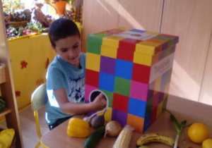 Chłopiec siedzi przy stoliku i wyjmuje warzywo z magicznego pudełka.